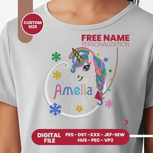 Puede incluir: Una camiseta gris claro con un diseño de unicornio colorido, una melena y un cuerno de arcoíris, y el nombre "Amelia" bordado en rosa. La camiseta incluye el texto "PERSONALIZACIÓN DE NOMBRE GRATUITA" y "TAMAÑO PERSONALIZADO".