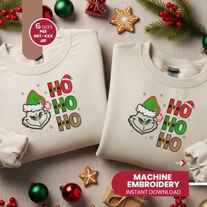 May include: Two cream-colored sweatshirts with a Grinch face and "HO HO HO" text in red, green, and brown. The sweatshirts are decorated with Christmas ornaments and greenery. The image also includes text that says "MACHINE EMBROIDERY INSTANT DOWNLOAD".