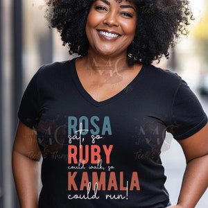 Könnte beinhalten: Ein schwarzes T-Shirt mit einem bunten Grafikdesign, auf dem "ROSA sat, so RUBY could walk, so KAMALA could run!" steht.
