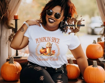 Può includere: Una t-shirt bianca a maniche corte con una stampa grafica di un latte alla zucca, una zucca intera e foglie autunnali. Il testo PUMPKIN SPICE SOCIAL CLUB è stampato in arancione sopra e sotto l'illustrazione centrale della bevanda.
