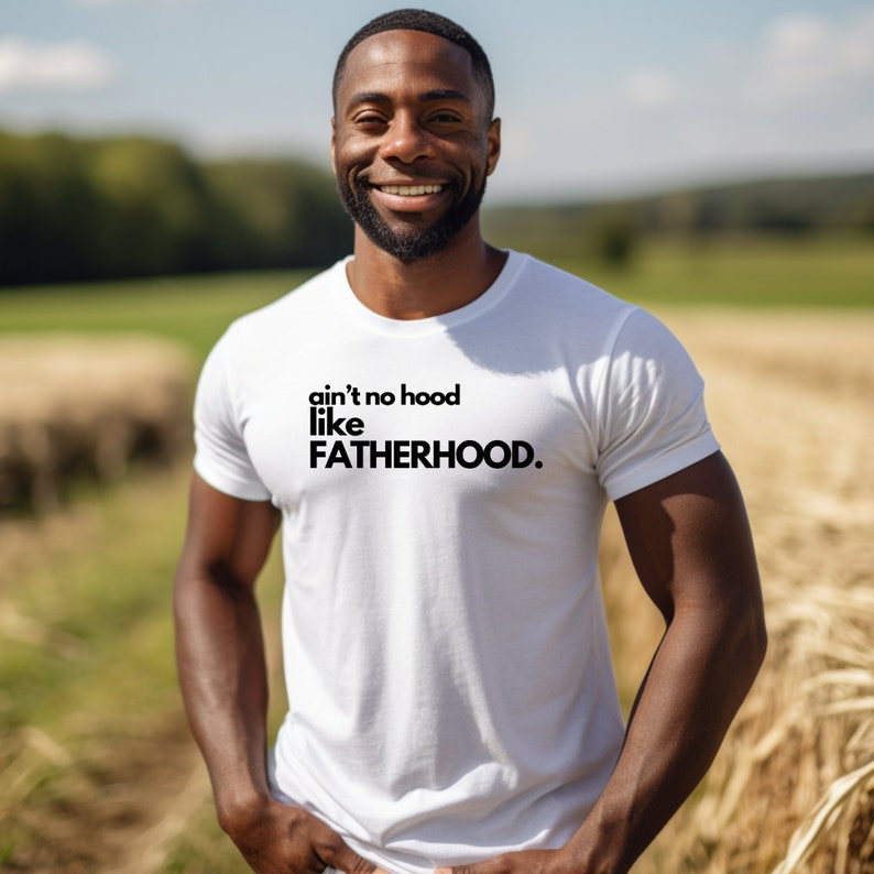 May include: White t-shirt with black text that reads "ain't no hood like FATHERHOOD."