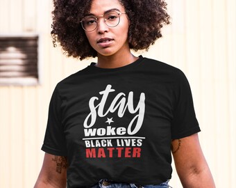Puede incluir: Camiseta negra con texto blanco que dice "stay woke black lives matter". La camiseta la lleva puesta una persona con el pelo rizado y gafas.