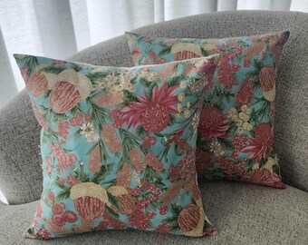 Könnte beinhalten: Zwei dekorative Kissen mit Blumenmuster. Die Kissen sind blaugrün mit rosa und goldenen Blumen. Die Kissen liegen auf einem grauen Sofa.
