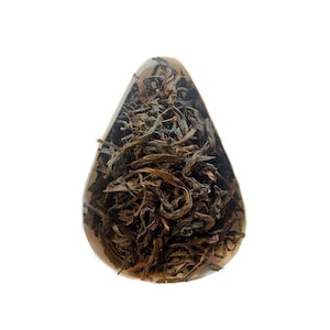 Può includere: Tè nero in foglie sfuse in una ciotola di ceramica bianca a forma di cucchiaio. Le foglie di tè sono di colore marrone scuro e verde.