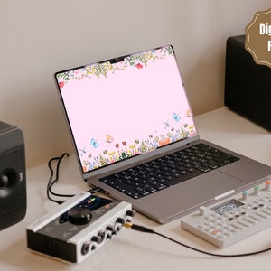 May include: A laptop computer with a pink background and a floral border with butterflies. The laptop is on a white desk with a black speaker, a white audio interface, and a white MIDI keyboard.