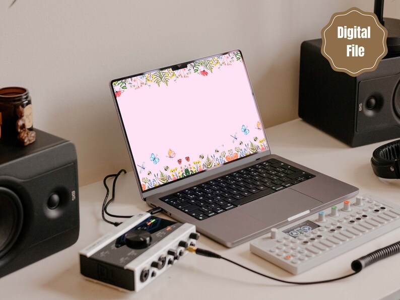 May include: A laptop computer with a pink background and a floral border with butterflies. The laptop is on a white desk with a black speaker, a white audio interface, and a white MIDI keyboard.
