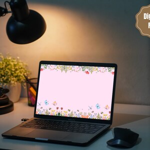 May include: A laptop computer with a pink background and a floral border on the screen. The border features butterflies, flowers, and leaves in shades of pink, blue, green, and yellow. The laptop is on a desk with a lamp and a plant in the background.