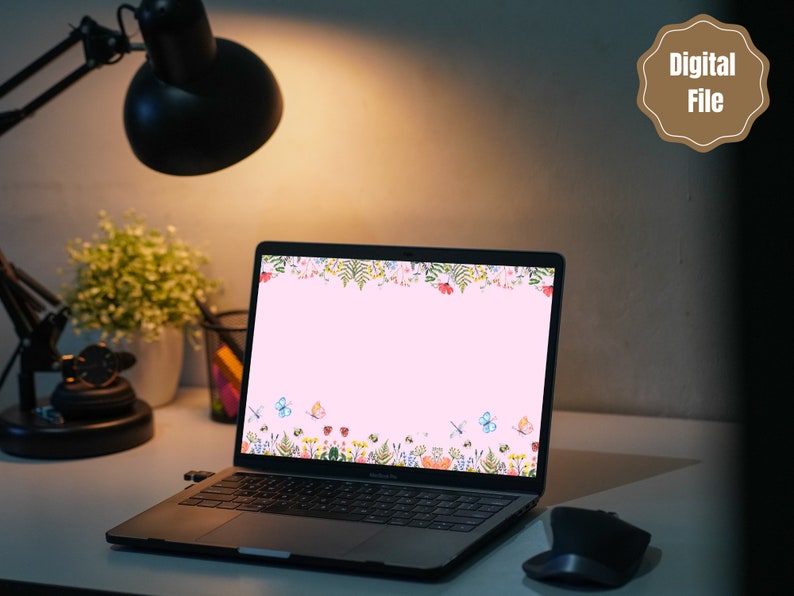 May include: A laptop computer with a pink background and a floral border on the screen. The border features butterflies, flowers, and leaves in shades of pink, blue, green, and yellow. The laptop is on a desk with a lamp and a plant in the background.