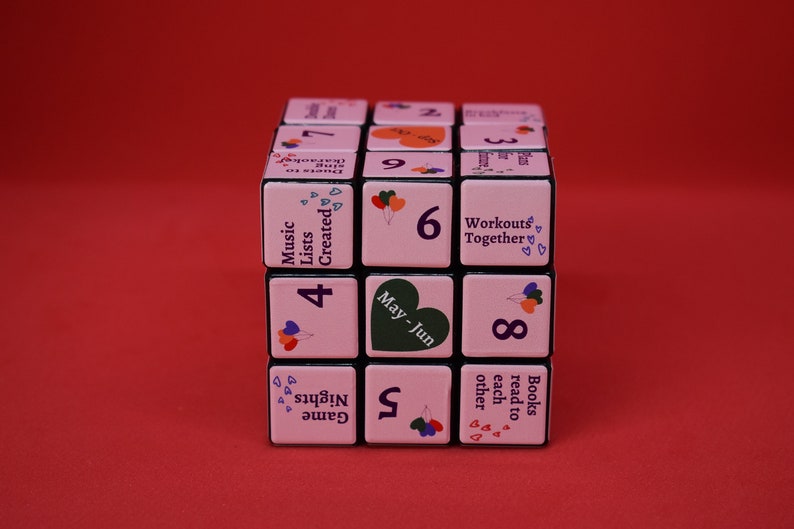 May include: A pink cube with black edges and numbers 1 through 9 on each side. Each side also has a different activity suggestion, such as "Music Lists Created", "Game Nights", "Books read to each other", "May-Jun", and "Workouts Together".