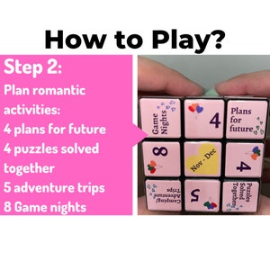 May include: A pink and black cube with different activities to plan for a romantic couple. The cube has numbers and text on each side, including "Game Nights", "Plans for future", "Puzzles Solved Together", "Adventure Trips", and "Nov-Dec".