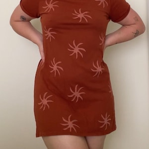 May include: A rust-colored short-sleeved dress with a pattern of pink stylized stars.