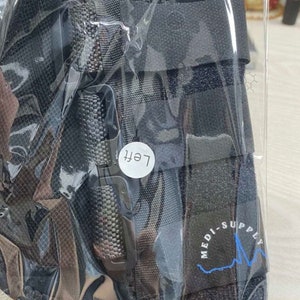 Puede incluir: Tobillera de soporte negra con cierre de velcro y una etiqueta que dice "Izquierda". La tobillera tiene un logotipo azul y blanco que dice "Medi-Supply".