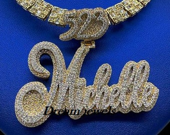 May include: Gold chain necklace with a large, custom-made pendant featuring the name "Michelle" and the number "528" set with clear cubic zirconia stones.