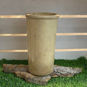 Może przedstawiać: Jasnobrązowy ceramiczny wazon stoi na kawałku drewna unoszącego się na wodzie, który umieszczony jest na sztucznej zielonej trawie.