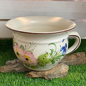 Peut inclure: Un pot en céramique blanche avec un bord brun et un motif floral. Le pot est posé sur un morceau de bois flotté sur un lit d'herbe artificielle verte.