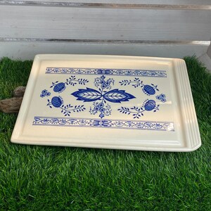 Pode incluir: Uma bandeja de servir de cerâmica branca com um design floral azul e branco. A bandeja tem uma borda elevada e é retangular.