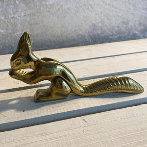 Op de afbeelding: Een gouden eekhoorn notenkraker. De eekhoorn zit met zijn staart achter zich opgerold. De notenkraker is gemaakt van metaal en heeft een gedetailleerd ontwerp.