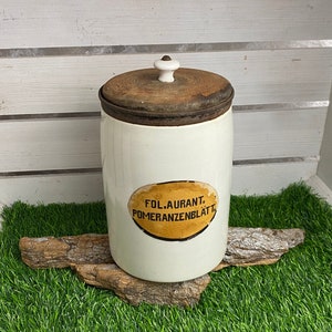 May include: White ceramic jar with a wooden lid and a yellow label that reads "Fol. Auranti. Pomeranzenblatt."