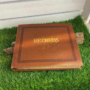 Puede incluir: Un álbum encuadernado en cuero marrón con letras doradas que dicen "RECORDS".