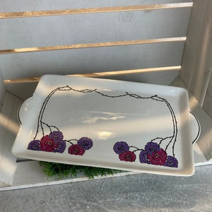 Puede incluir: Bandeja rectangular blanca para servir con diseño floral negro y flores rosas y moradas. La bandeja tiene dos asas a los lados.