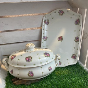 Könnte beinhalten: Eine weiße Porzellanservierschale mit Blumenmuster und passendem Deckel. Die Schale hat einen goldenen Rand und ist mit rosa und violetten Blumen verziert.