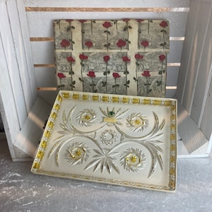 Può includere: Un vassoio da portata in vetro bianco con un bordo giallo e un design a taglio di foglie e fiori. Il vassoio è appoggiato su una superficie bianca.