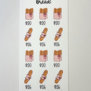 May include: A white sticker with the text "making that bread" in cursive. The sticker features illustrations of bread loaves and baguettes, each with a price tag. The bottom of the sticker has the text "Ts Budgets".