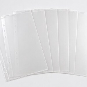 May include: A set of clear, rectangular plastic sheet protectors arranged in a fan shape. Each sheet features a reinforced vertical edge with a series of punched circular holes designed for insertion into a standard ring binder or planner system.