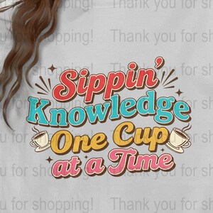 May include: White sweatshirt with the text "Sippin' Knowledge One Cup at a Time" in retro colors. The design includes coffee cups and starburst accents, perfect for coffee lovers and those who enjoy a cozy aesthetic.