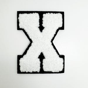 May include: White chenille letter "X" patch with a black border. The letter has a fluffy texture and is centered on a white background. This patch is suitable for jackets, bags, or other fabric items.