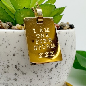 May include: A gold pendant necklace with a rectangular tag that reads "I am the fire storm XXX".