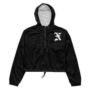 May include: Black cropped anorak jacket with a hood and a white interior lining. The jacket features a white gothic-style letter "A" on the front. It has a drawstring at the hem and a half-zip closure.