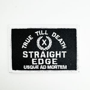 Pode incluir: Etiqueta bordada preta e branca com o texto "True Till Death Straight Edge Usque Ad Mortem" e uma coroa com um "X" no centro.