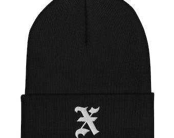 Op de afbeelding: Zwarte beanie met een wit geborduurde letter "X" op de voorkant. De beanie is gemaakt van een zacht, gebreid materiaal en heeft een omgeslagen rand. Een warm en stijlvol winteraccessoire.