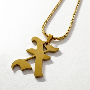 May include: Gold-colored pendant necklace featuring a stylized letter "A" with an attached chain. The pendant has a unique, artistic design with curved and angular elements. The chain is a delicate, textured gold color.