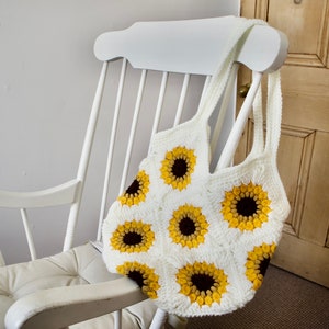 Puede incluir: Una bolsa de mano de crochet blanca con un patr&oacute;n de girasol. La bolsa est&aacute; colgada de una mecedora blanca.