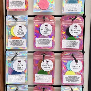 May include: Twelve holographic pouches containing vacuum freshener discs, each labeled with scents like Dark Opium, Lemongrass Tea, Coconut Creme, Baby Powder, Creed For Him, Raspberry Ripple, Ocean Breeze, Sandalwood Vanilla, Sauvage, Cherry Bakewell, Coco Madam, and Clean Linen.