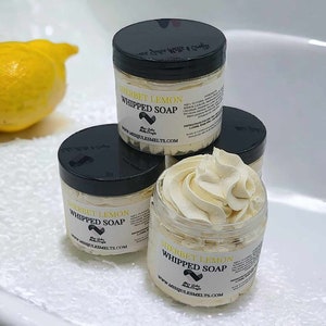 Puede incluir: Tres frascos de jabón batido de limón sorbet con tapas negras. Los frascos están sobre una superficie blanca. El jabón es de color amarillo claro y tiene una textura batida. Los frascos tienen una etiqueta que dice "Sherbet Lemon Whipped Soap" y "www.missjulesmelts.com".