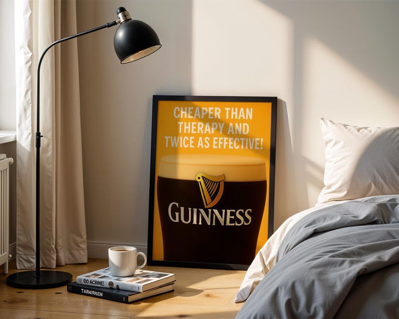 Może przedstawiać: Oprawiony plakat Guinness z napisem &bdquo;Tańsze niż terapia i dwa razy skuteczniejsze!&rdquo;. Czarna lampa podłogowa i biały kubek na książkach są na pierwszym planie. Plakat przedstawia kufel Guinnessa.
