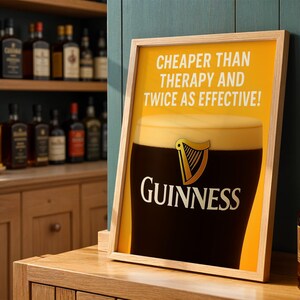 Może przedstawiać: Oprawiony plakat z logo Guinness i kuflem stoutu. Plakat zawiera tekst "CHEAPER THAN THERAPY AND TWICE AS EFFECTIVE!" na ż&oacute;łtym tle. Rama jest jasnobrązowa.