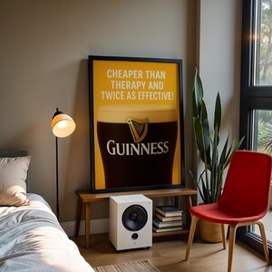 Może przedstawiać: Oprawiony plakat Guinness z napisem "Cheaper than therapy and twice as effective!". Biały głośnik, stos książek, czerwone krzesło i lampa podłogowa r&oacute;wnież znajdują się w pokoju.