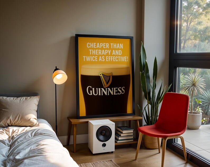 Może przedstawiać: Oprawiony plakat Guinness z napisem "Cheaper than therapy and twice as effective!". Biały głośnik, stos książek, czerwone krzesło i lampa podłogowa r&oacute;wnież znajdują się w pokoju.