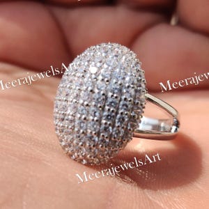 Könnte beinhalten: Eine weiße Keramik-Tasse mit schwarzem Henkel und dem Text "But First, Coffee" in fetter, schwarzer Schrift. Die Tasse steht vor einem verschwommenen Hintergrund, der eine gemütliche Umgebung suggeriert.