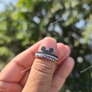 K&ouml;nnte beinhalten: Ein stapelbares Ring-Set bestehend aus drei Ringen. Der oberste Ring zeigt eine mit schwarzen Steinen besetzte Mausohr-Silhouette, der mittlere Ring ist eine d&uuml;nne Reihe klarer Steine und der untere Ring besteht aus einer Reihe runder roter Steine.