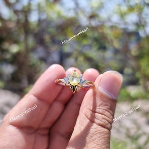 May include: A gold ring featuring a central pear-cut yellow gemstone flanked by small clear stones in a pointed setting. The band is thin and metallic. The text Meerajewelsart is visible on the image. The design includes a star-like metal base.