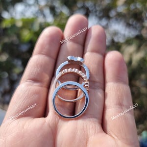 May include: A stack of three rings featuring a silver-toned band with a decorative top, a rose gold-toned band with a scalloped edge, and a plain silver-toned band. The text Meerajewelsart is visible in the image.