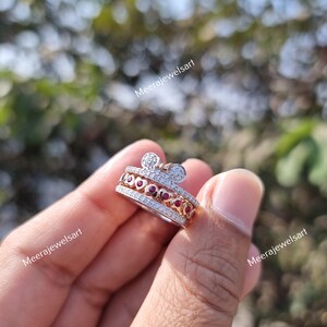 May include: A silver-toned ring featuring a band with a row of small clear stones, a central row of red heart-shaped stones, and a top section shaped like a mouse head with clear stones. The text Meerajewelsart is visible on the image.