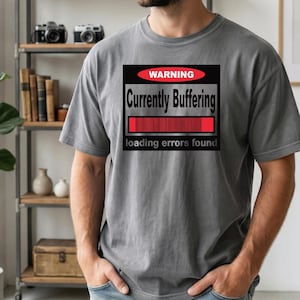K&ouml;nnte beinhalten: Ein anthrazitfarbenes Kurzarm-T-Shirt mit einer rechteckigen Grafik, die ein rotes Oval mit dem Wort WARNING, den Text Currently Buffering, einen roten Ladebalken und den Text loading errors found am unteren Rand enth&auml;lt.
