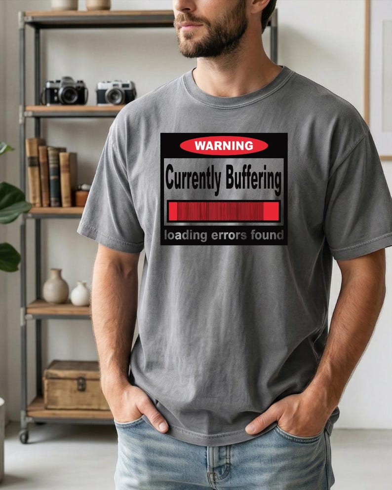 K&ouml;nnte beinhalten: Ein anthrazitfarbenes Kurzarm-T-Shirt mit einer rechteckigen Grafik, die ein rotes Oval mit dem Wort WARNING, den Text Currently Buffering, einen roten Ladebalken und den Text loading errors found am unteren Rand enth&auml;lt.