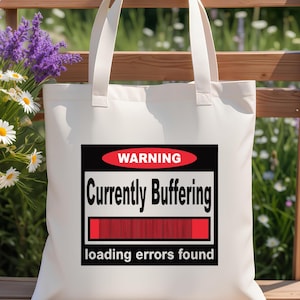 K&ouml;nnte beinhalten: Eine wei&szlig;e Stofftasche mit einer rechteckigen Grafik, die ein rotes Oval mit dem Wort WARNING, den schwarzen Text Currently Buffering, einen roten Ladebalken und den Text loading errors found am unteren Rand enth&auml;lt.